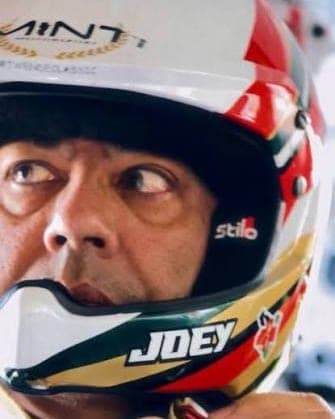 Joey Ghose in the car, eyes up, fastening the strap of his Minti-liveried helmet with JOEY across the chin bar
