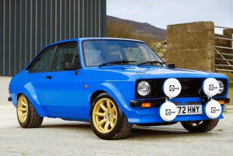 Escort Mk2 rally build in blue with gold Minilite-style wheels and Cibie spotlamps outside the workshop
